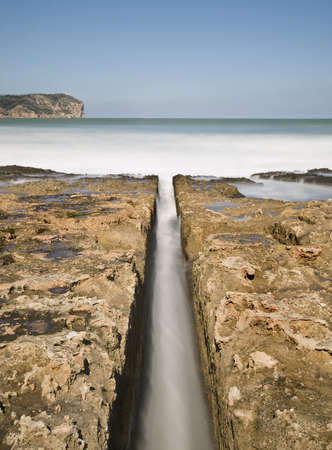 Seascape with a channel in the center of the image bearing seawater through the rocks to the breaking waves on the shore. の写真素材