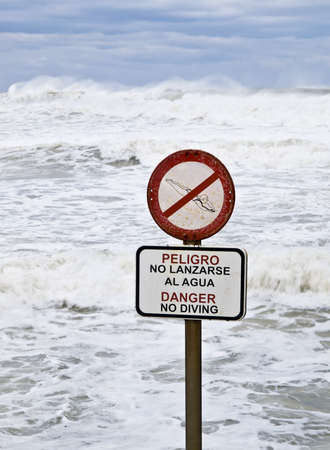 Danger No Diving sign with a stormy sea in the background. Signal written in Spanish and Englishの写真素材