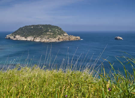 Seascape seen from the top of a cliff above the sea with two islands on the horizon and the fresh green grass in the foreground.の写真素材