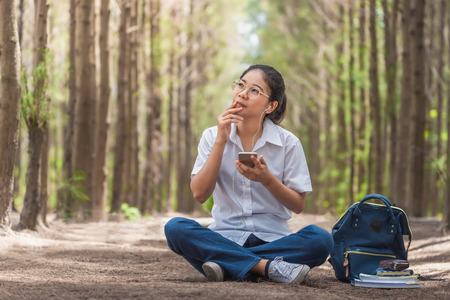 Smiling woman using a smart phone and relaxing at the park on grass. -の写真素材