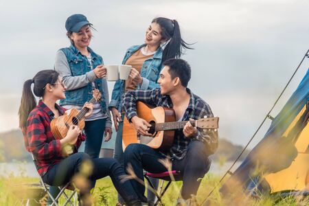 Group of Asian friends having fun eating barbecue outdoor while camping and play guitar.の写真素材