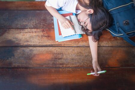 tired student girl with books and bag sleeping on the table. education, session, exams and school concept . studying hard. Top viewの写真素材