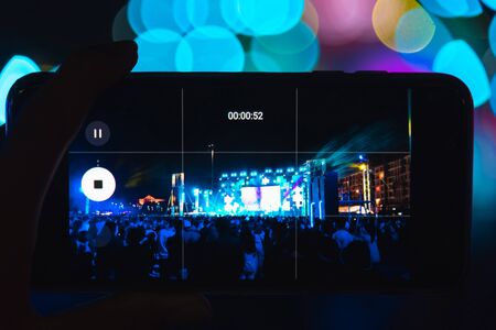 Blurred girl hands making video of summer festival concert with mobile phone - Crowd celebrating party event - Defocused image - Concept of fun, music and entertainment - Original color lightsの写真素材