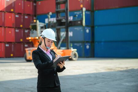 Asian woman engineer use check sheet for control loading Containers box from Cargo freight ship for import and exportの写真素材