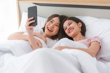 Young pretty happy woman laying down in bed with mobile phoneの写真素材