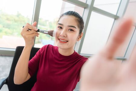 Famous blogger. Cheerful female vlogger is showing cosmetics products while recording video and giving advices for her beauty blog. Focusl camera selfie viewの写真素材