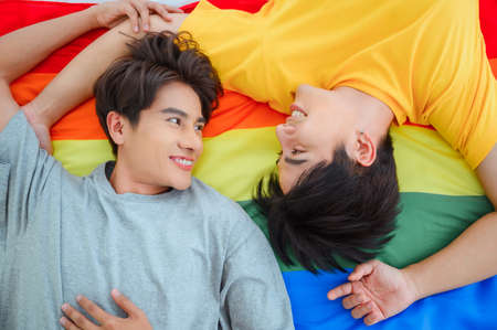 Young gay couple lying on bed in bedroom. Enjoying in morning. Wearing pajamas. asian ethnicity, black hair.の写真素材