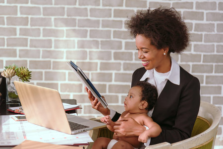 Black mother is raising a child and working on a laptop together at home.
