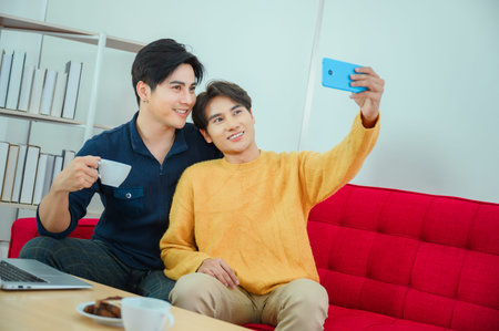 LGBQ concept of sexual diversity Gay Asian couple use their phones to take fun photos together in their room.の写真素材