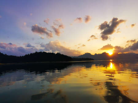 Sun piercing the sky to start the day with islands and lake in the foregroundの写真素材