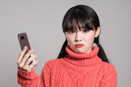 Studio portrait of twenties Asian women annoyed by phoneの写真素材