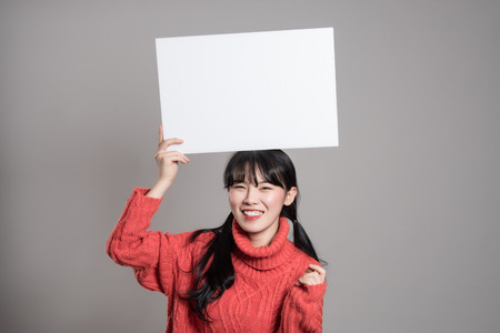 A studio portrait of a twenties Asian woman holding a billboard with a happy smileの写真素材