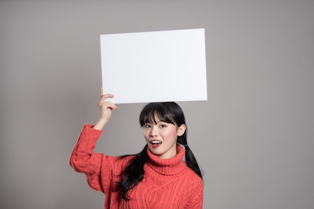 A studio portrait of a twenties Asian woman holding a billboard with a happy smileの写真素材
