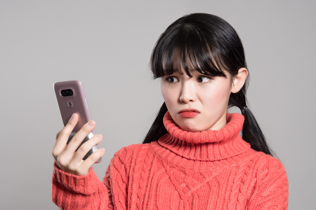 Studio portrait of twenties Asian women annoyed by phoneの写真素材