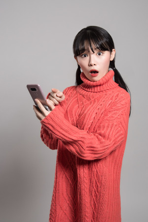 A studio portrait of a twenties Asian woman with a surprised look on the phoneの写真素材