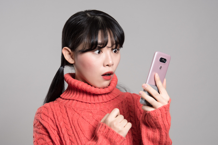 A studio portrait of a twenties Asian woman with a surprised look on the phoneの写真素材