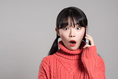 A studio portrait of a twenties Asian woman with a surprised look on the phoneの写真素材