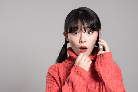 A studio portrait of a twenties Asian woman with a surprised look on the phoneの写真素材