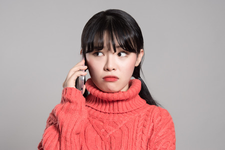 Studio portrait of twenties Asian woman receiving an unknown callの写真素材