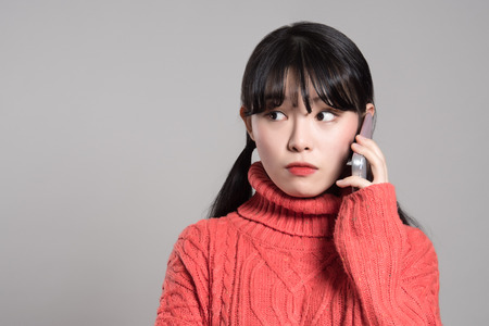 Studio portrait of twenties Asian woman receiving an unknown callの写真素材