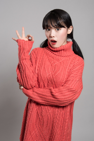 A studio portrait of a twenties Asian woman pointing at something with a finger and looking surprisedの写真素材