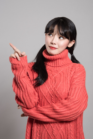 A studio portrait of a twenties Asian woman pointing at something with a finger and being happyの写真素材