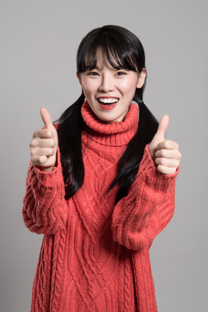 Studio portrait of twenties Asian woman of happy appearance holding thumb upの写真素材