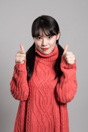 Studio portrait of twenties Asian woman of happy appearance holding thumb upの写真素材