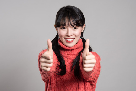 Studio portrait of twenties Asian woman of happy appearance holding thumb upの写真素材