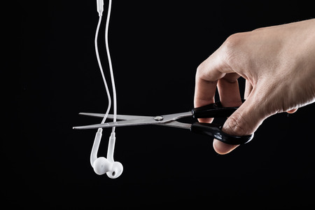 Scissors to cut earphones. Black backgroundの写真素材