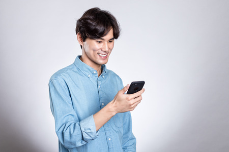 Studio portrait of a handsome asian man holding a smart phoneの写真素材
