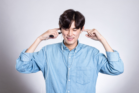 Studio portrait of joyful asian man with smart phone and musicの写真素材