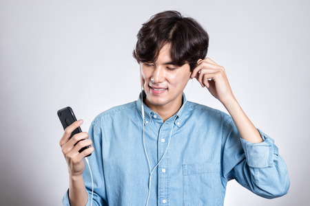 Studio portrait of joyful asian man with smart phone and musicの写真素材
