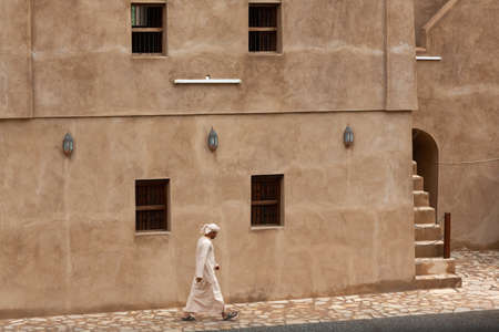 Omani in traditional dishdasha dress walking along wall of Jibreen Castle, Omanのeditorial素材
