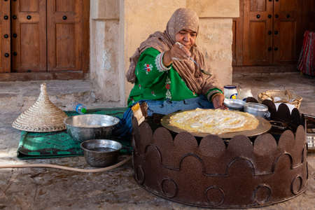 Omani woman in traditional dress preparing a crispy crepe in Nizwa's fortのeditorial素材