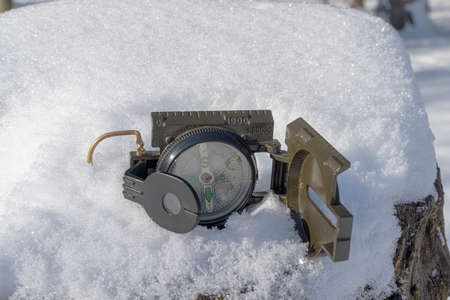 Opened, green compass lies in the fresh snow. The compass has sunk slightly into the snow.の写真素材