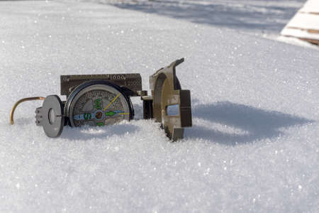 Opened, green compass lies in the fresh snow. The compass has sunk slightly into the snow.の写真素材