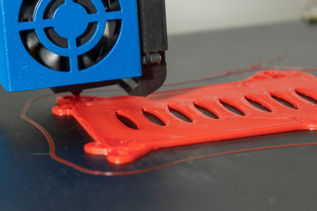 Close-up of a 3D printer printing a red plastic figure