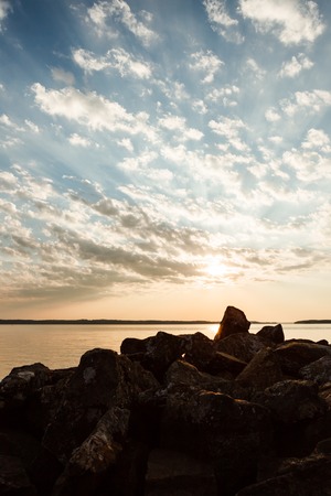 Beautiful clouds and sun rays over lake and rocks at sunriseの写真素材