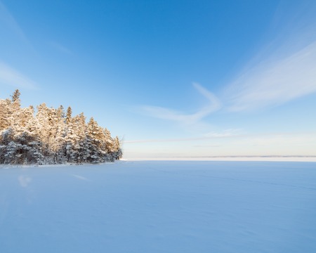 Frozen lake and snow covered forest at cold sunny winter day in Finlandの写真素材