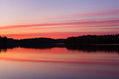 Serene view of calm lake and tree silhouettes at twilightの写真素材