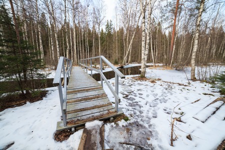 Small wooden bridge over partially frozen forest river at spring in finlandの写真素材