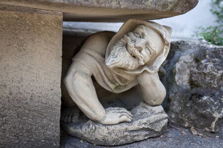 Funny looking human statue crouching under bench in gardenの写真素材