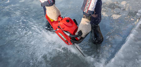 Russia, River Volga Kama - Jan 17th 2020. Man carving an ice hole entry with a motor saw chainsaw for ice scuba divingの写真素材