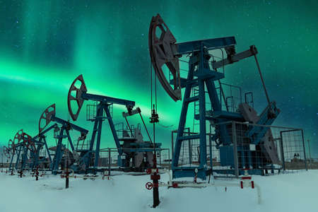 Oil pump - Nodding donkey. Night view. Oil industry equipment. Oil field pump jack and oil refinery in the winter with snow, mountains and forest in background.の写真素材