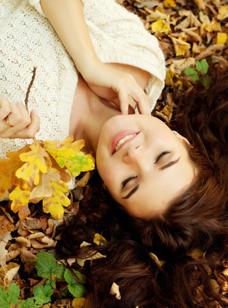 woman lying on autumn leaves, outdoor portraitの写真素材