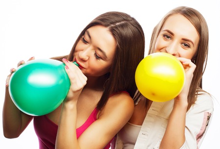 Two happy hipster girls smiling and holding colored balloons over white backgroundの写真素材