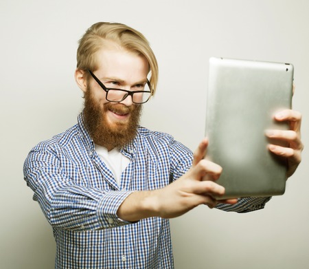 life style, tehnology and people concept: Happy selfie. Young bearded man holding tablet and making photo of himself while standing against white backgroundの写真素材