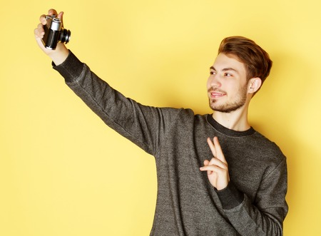 Portrait of a smiling man making selfie photo over yellow backgroundの写真素材