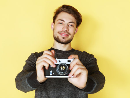 Say cheese! Handsome young man looking at camera while standing against yellow background
